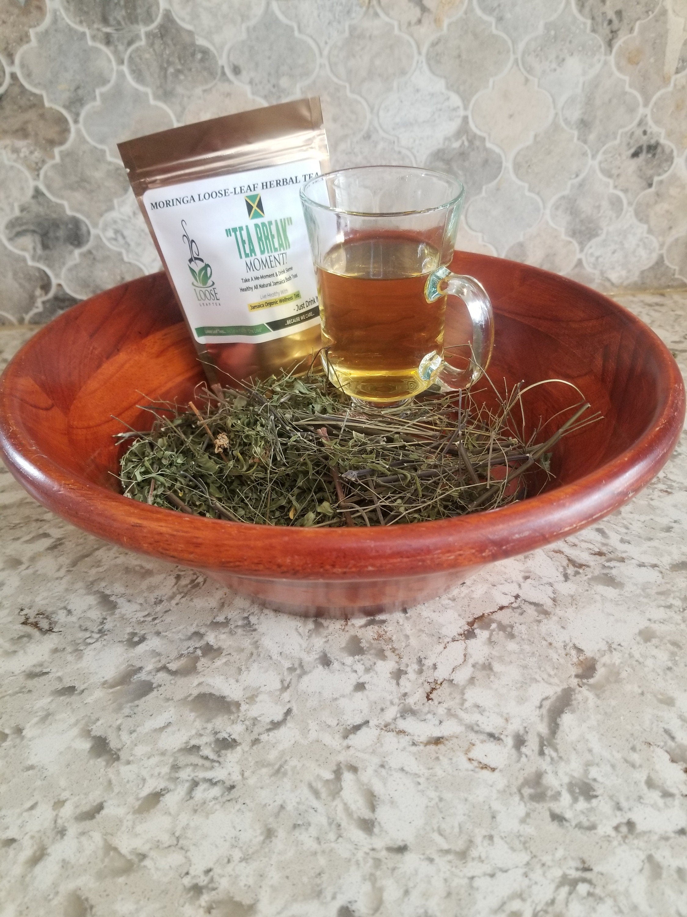 Moringa tea leaves in a wooden bowl beside a cup of tea